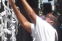 A woman at the Trinity Church gates, ties a  ribbon to respect and honor those lost on 9/11. Thousands of people came to pay their respects and to remember the tragedy that befell NYC 20 years ago. 

An array of events were scheduled throughout NYC to honor and remember the catastrophe that shook the world in 2001. September 11, 2021 (C)Bianca Otero