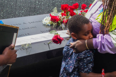 A boy hugs his mother as his family place flowers and make a pencil rubbing of the name of their lost family member at the North Pool of the 9/11 memorial. 
Hundreds of people came to the memorial to pay tribute to their family members and loved ones marking the 20th anniversary of the tragedy that struck NYC and shocked the world on 9/11/01. (C) Bianca Otero