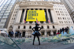 NEW YORK, NEW YORK - MARCH 08: People walk past a broken glass ceiling installation in front of the Fearless Girl Statue in front of the New York Stock Exchange on International Women's Day on March 08, 2021 in New York City. The art installation by Global Street Global Advisors celebrates women who have made a difference for all "Fearless Girls."  (Photo by Alexi Rosenfeld/Getty Images)
