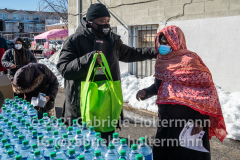 A volunteer assists a woman at a community food drive in Jamaica, Queens, on Feb. 4, 2021. (Photo by Gabriele Holtermann for Queens Courier)