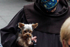 A Friar from the Church of St. Francis of Assisi in NYC stands with his little dog in hand awaiting visitors with their furry family for the Blessing of Animals that takes place every year on the first Sunday of October. 
In the Roman Catholic Church, St. Francis of Assisi is patron saint of animals, merchants and ecology.
People from all over bring their beloved furry and not so furry companions to receive blessings. This year broke an all time record of attendees who seek better horizons and better health for the upcoming year. (C) Bianca Otero, NYC. October 3, 2021.