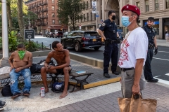 Two NYPD officers look on while Curtis Sliwa, founder of the Guardian Angels, and his crew speak to a group of  unsheltered men while patroling the Upper West Side in New York City on August 9, 2020.  The neighborhood has experienced an uptick in crime and drugs after hotels have been turned into homeless shelters. (Photo by Gabriele Holtermann)