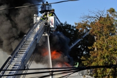 Firefighters operate as heavy fire vents through the roof of a one story building. (Photo by Lloyd Mitchell)