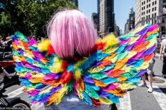 A woman with a pink wig and rainbow colored wings on a motorcycle at the New York City Pride March.
