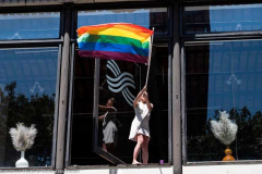 A woman waving a rainbow flag in a window overlooking the New York City Pride March.