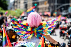 A woman with a pink wig and rainbow colored wings on a motorcycle at the New York City Pride March.