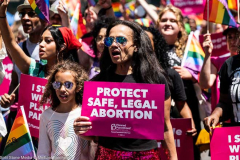 A woman with a t-shirt saying "1973" and a sign saying "Protect safe, legal abortion - Planned Parenthood" marching with the Planned Parenthood group at the New York City Pride March.