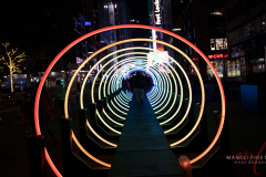 PASSAGE is an immersive, minimalist, contemplative and interactive artwork that explores the emotional connections we develop with light and sound. The concept of the artwork takes root in the definition of the word passage itself: the act of moving through or past something on the way from one place to another, and also the process of transition from one state to another in a temporal dimension. The installation consist of circles of light that form a tunnel which bystanders will go through a sound system. The passage through the tunnel activities light animations and sounds. Each configuration has its own ambiance. The creator of this installation is Serge Maheu and the owner is Iluminart. This interactive artwork will be view through 13 February 2022 in New York City